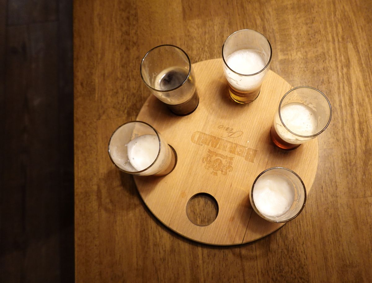 Overhead view of five beer glasses arranged in a tasting flight on a round wooden tray