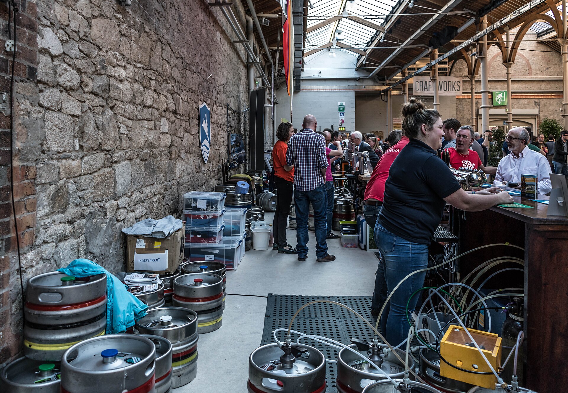 Brewers serving a crowd beside stacked kegs at a craft beer festival