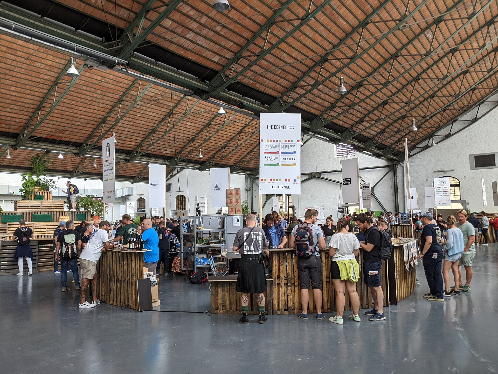 Beer festival guests gathered around tasting stands in a market hall